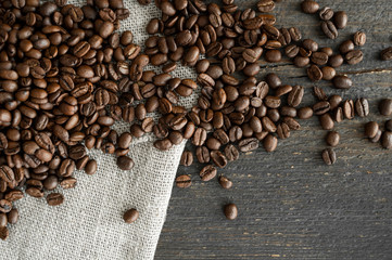 Coffee beans on a linen textile and on a wooden table background. Fresh arabica coffee beans.