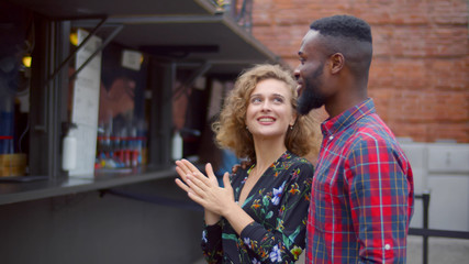 Young multiethnic couple choosing meal standing near food truck on street