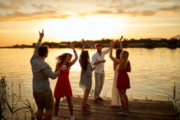 Group of friends dancing on the party with a beautiful sunset on the lake