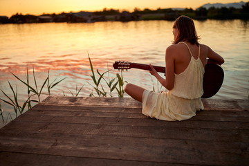 Young girl playing guitar on the lake