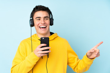 Teenager caucasian man isolated on purple background listening music with a mobile and singing