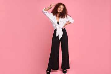 Full length photo of cute positive girl showing v-sign isolated on pastel pink background.