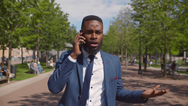 Young african angry businessman talking on phone with difficult client walking outdoors