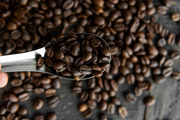 Fresh roasted arabica coffee beans in a metal spoon and scattered coffee beans on a wooden table.