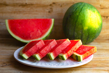 Fresh ripe red watermelon. The whole and cut in pieces on plate on wooden background