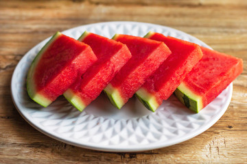 Slices of fresh ripe watermelon, cut in pieces on white plate on wooden background
