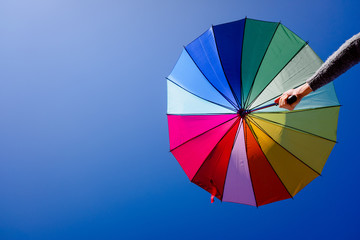 Obraz premium Woman holds a multicolored parasol on a summer day with blue sky background.