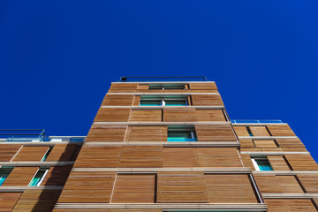 A tall building with a wooden facade to be more ecological and sustainable in its construction and maintenance, seen from below with a sky background.