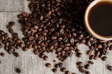 Koffiekopje met gebrande koffiebonen op linnen achtergrond. Mok zwarte koffie met verspreide koffiebonen. Verse koffiebonen.