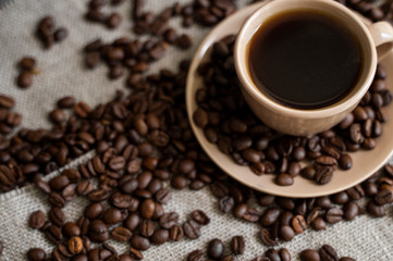 Coffee cup with roasted coffee beans on linen background. Mug of black coffe with scattered coffee beans. Fresh coffee beans.
