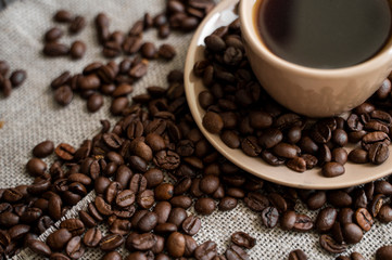 Coffee cup with roasted coffee beans on linen background. Mug of black coffe with scattered coffee beans. Fresh coffee beans.
