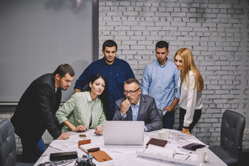 Management team of male and female professionals watching presentation of new project on laptop computer connecting to wireless high speed internet during working process in office interior