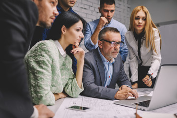 Group of pondering skilled marketing experts searching useful information in websites on laptop computer connected to wireless internet while creating new advertising campaign on formal meeting