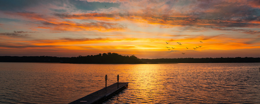 Colorful; sunrise over a serine lake with reflections, sunrays, and birds in flight.