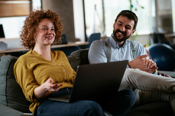 Businesswoman and businessman sitting and talking in office. Young woman and man working on laptop.
