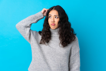 Fototapeta premium Spanish Chinese woman over isolated blue background having doubts while scratching head