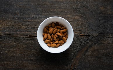 Almonds in a small plate on a vintage wooden table. Almond is a healthy vegetarian protein nutritious food. Natural nuts snacks.