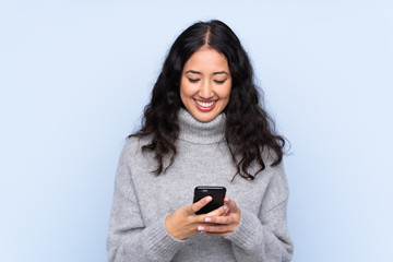 Spanish Chinese woman over isolated blue background sending a message with the mobile