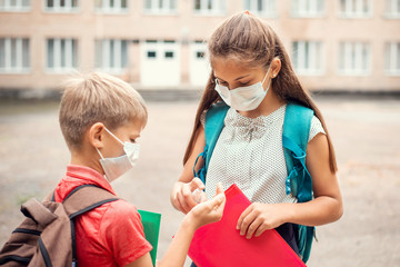 Elder sister applying hand sanitizer to her small brother to clean hands before the classes, concept of education during the coronavirus pandemic