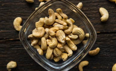 Cashew nuts in a small plate with scattered cashew around a plate on a vintage wooden table as a background. Cashew nut is a healthy vegetarian protein nutritious food.