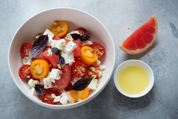 Grapefruit, feta cheese and tomato salad served in a white bowl, studio shot on a light-blue stone background, elevated view