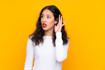 Mixed race woman over isolated yellow background listening something