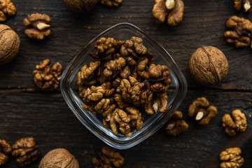 Walnut in a smale plate with scattered shelled nuts and whole nut which standing on a wooden vintage table. Walnuts is a healthy vegetarian protein nutritious food. Walnut on rustic old wood.
