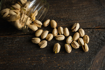 Pistachios scattered on the vintage table from a jar. Pistachio is a healthy vegetarian protein nutritious food. Pistachios on rustic old wood.