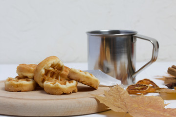 Mug of tea and waffles. Nearby on the table are dried maple leaves, a tea bag and dried oranges. Autumn still life.