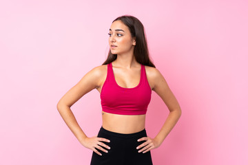 Young sport girl over isolated pink background posing with arms at hip and looking side