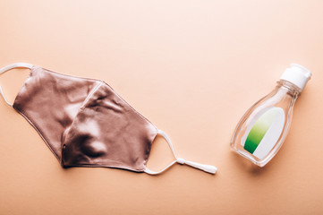 New normal with reusable silk face mask and hand cleanser gel on dusty pink background