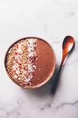 Chocolate Smoothie from Banana and Strawberries with cacao, Granola and Coconut Shreds on top in Coconut Shell Bowl, strong shadows. Healthy summer breakfast, top view
