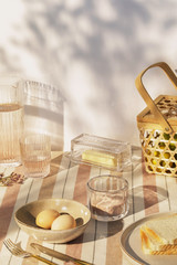 Stylish composition of outdoor kitchen space with wooden table, food, drinks, kitchen accessories, beige tablecloth and summer shadows. Country side mood. Template.