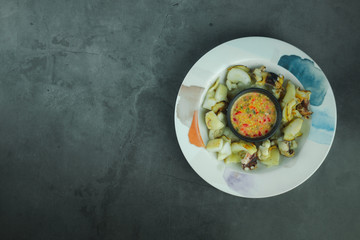 Grill squid served with a spicy sauce in dish on a black background