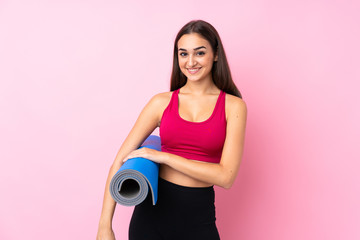 Young sport girl over isolated pink background with a mat and smiling