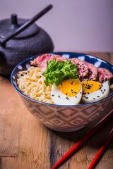 Ramen Soup with Wagyu Beef Filet in Bowl on wooden table. Beef ramen served Asian style. Raw egg cooks in steaming hot savory broth.