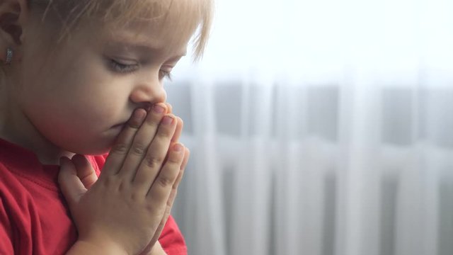 little daughter girl makes a wish prayers bedtime religion concept . prayer child indoors praying by lifestyle bed front of window