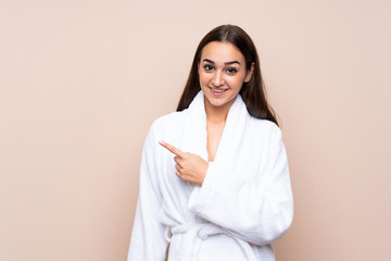 Young girl in a bathrobe over isolated background pointing finger to the side