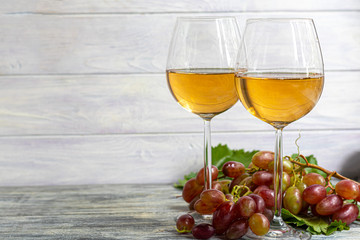 Large and light, wine grapes. It is covered with a white coating called yeast. Glasses are filled with light wine. Water drops on berries. On a wooden background.