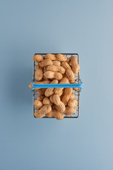 Roasted unpeeled peanuts in shell in shopping basket isolated on blue background. Food, ingredients, organic vegetarian protein, healthy and dietary nutrition concept. Top view with copy space.