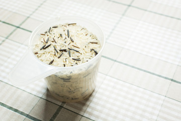 White and brown rice in measuring cup on kitchen table.