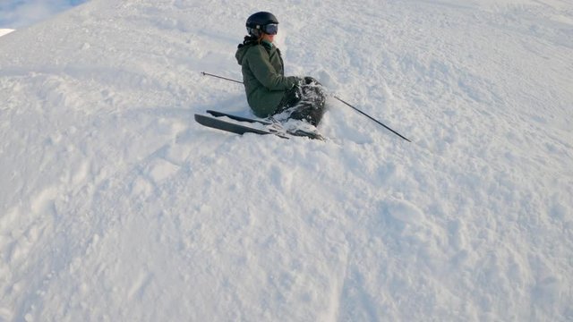 Female skier descends a ski slope, falls foolishly and smiles at the camera. It's a sunny winter day in spanish Pyrenees.