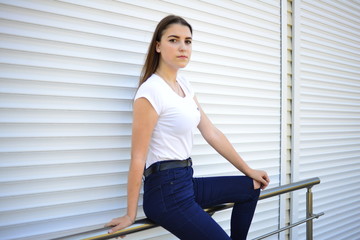 Beautiful young woman wearing jeans, white t-shirt, standing on the street. photo near iron fence