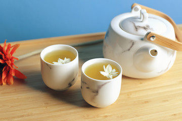 Two small teacups and a teapot with jasmine flowers. All on a wooden tray