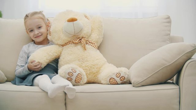 4k video of little blonde girl hugging big plush teddy bear.