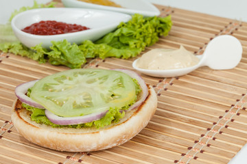 Slice Of Bread For Hamburger With Vegetables: Green Tomato, Lettuce And Onion Rings; Ready To Assemble The Burger.