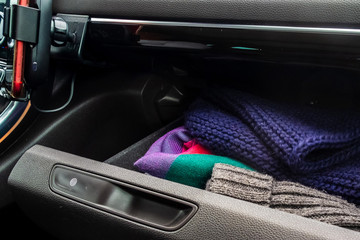 Knitted scarves and hats are in the glove compartment of a car.
