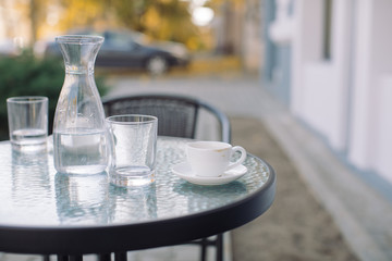 Jug, glass of water and cup of coffee on table at terrace. Outdoors, copy space.