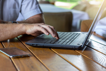 Shot of an unrecognizable man using a laptop while working from home. Men is typing on laptop computer keyboard. Close up of a male using a computer. Hands of business person working on computer.