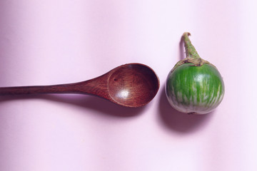 Conceptual photo of a kermit eggplant and wooden spoon on a pink background to show concept of wellness, veganism, clean living and  nutrition